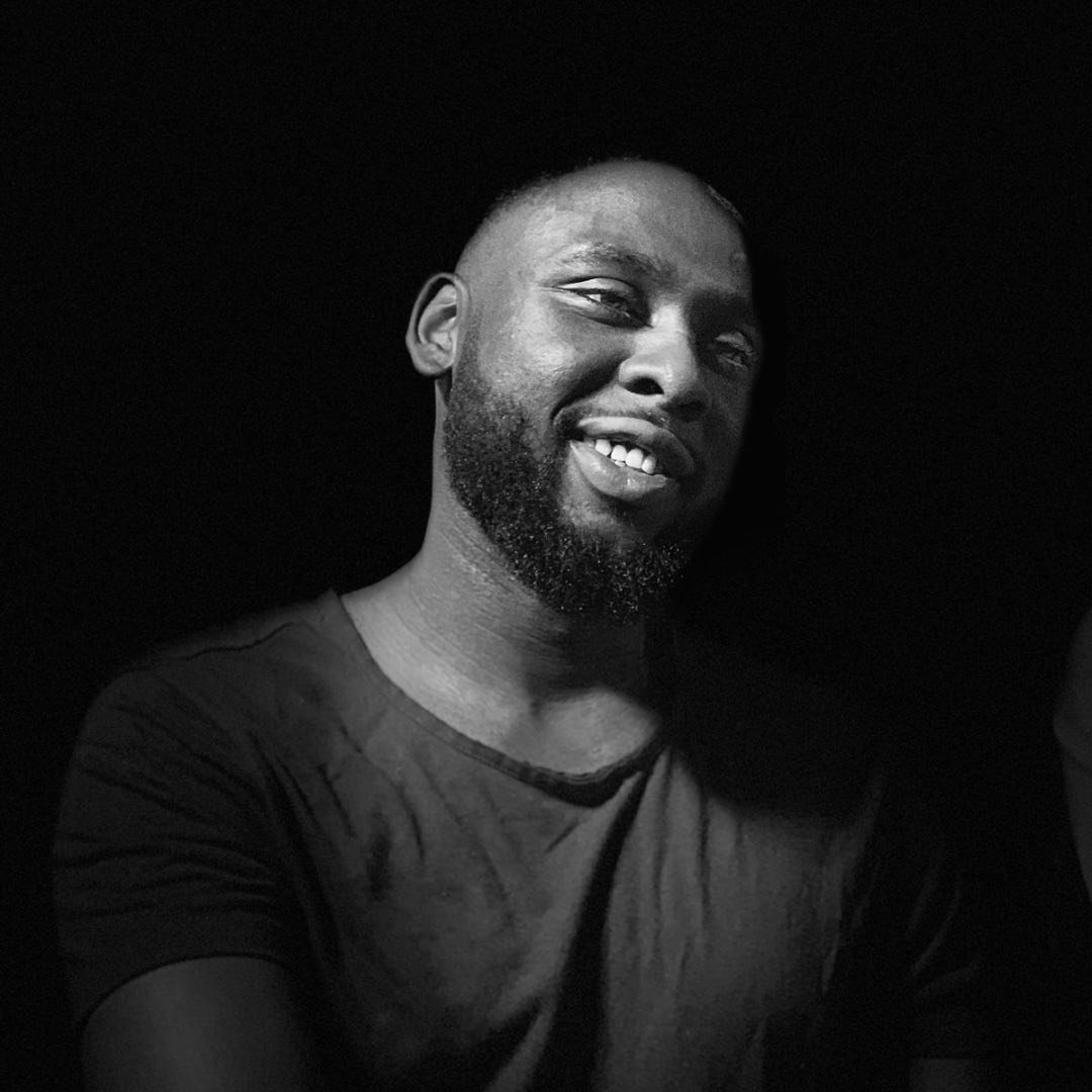 Yahya Abbakar smiling away from the camera in dark background